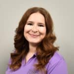 Motivational woman healthcare professional smiling at camera wearing purple scrubs with BHP embroidery, representing trusted business health partners, focus on employee wellness and healthcare solutions, HR, and employee health management.